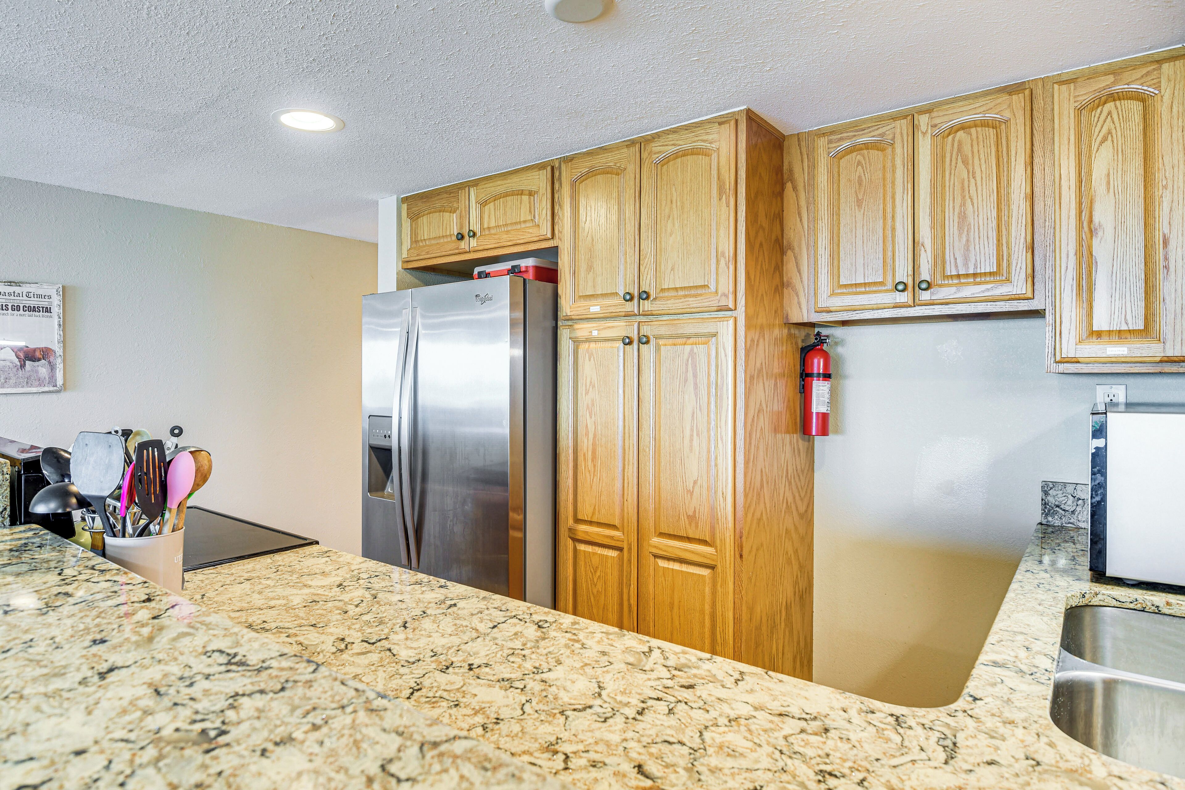 A kitchen with wooden cabinets, a stainless steel refrigerator, and a granite countertop.