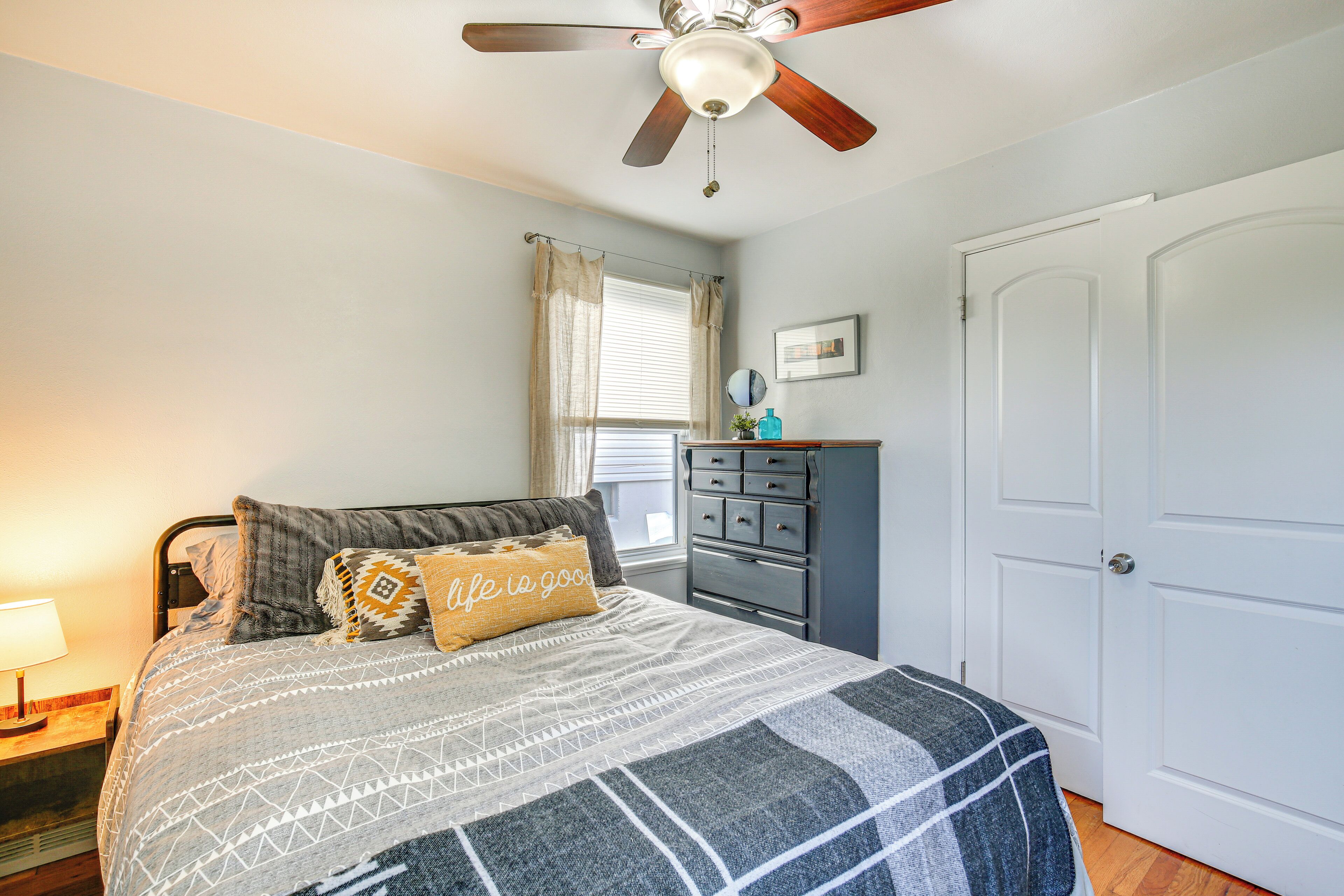 A bedroom with a bed, a ceiling fan, a dresser, and a door.