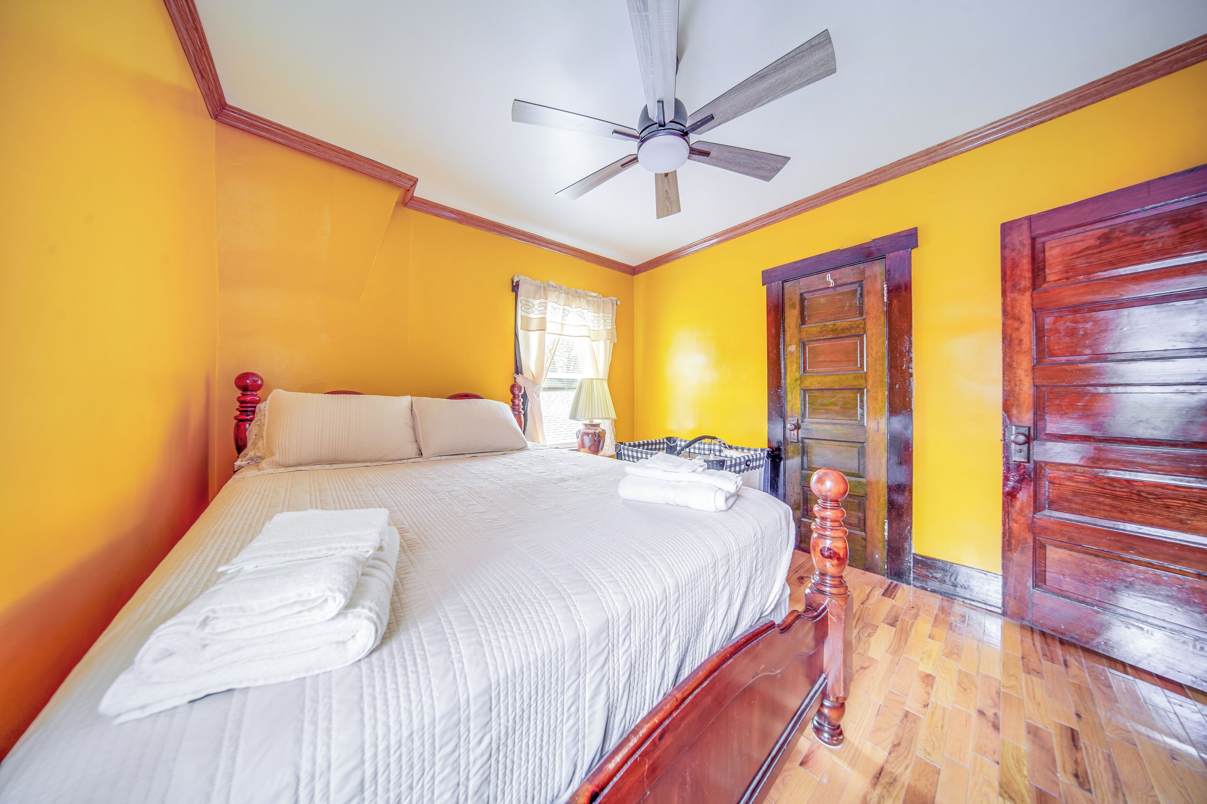 A bedroom with a bed, a ceiling fan, a wooden door, and a window with curtains.