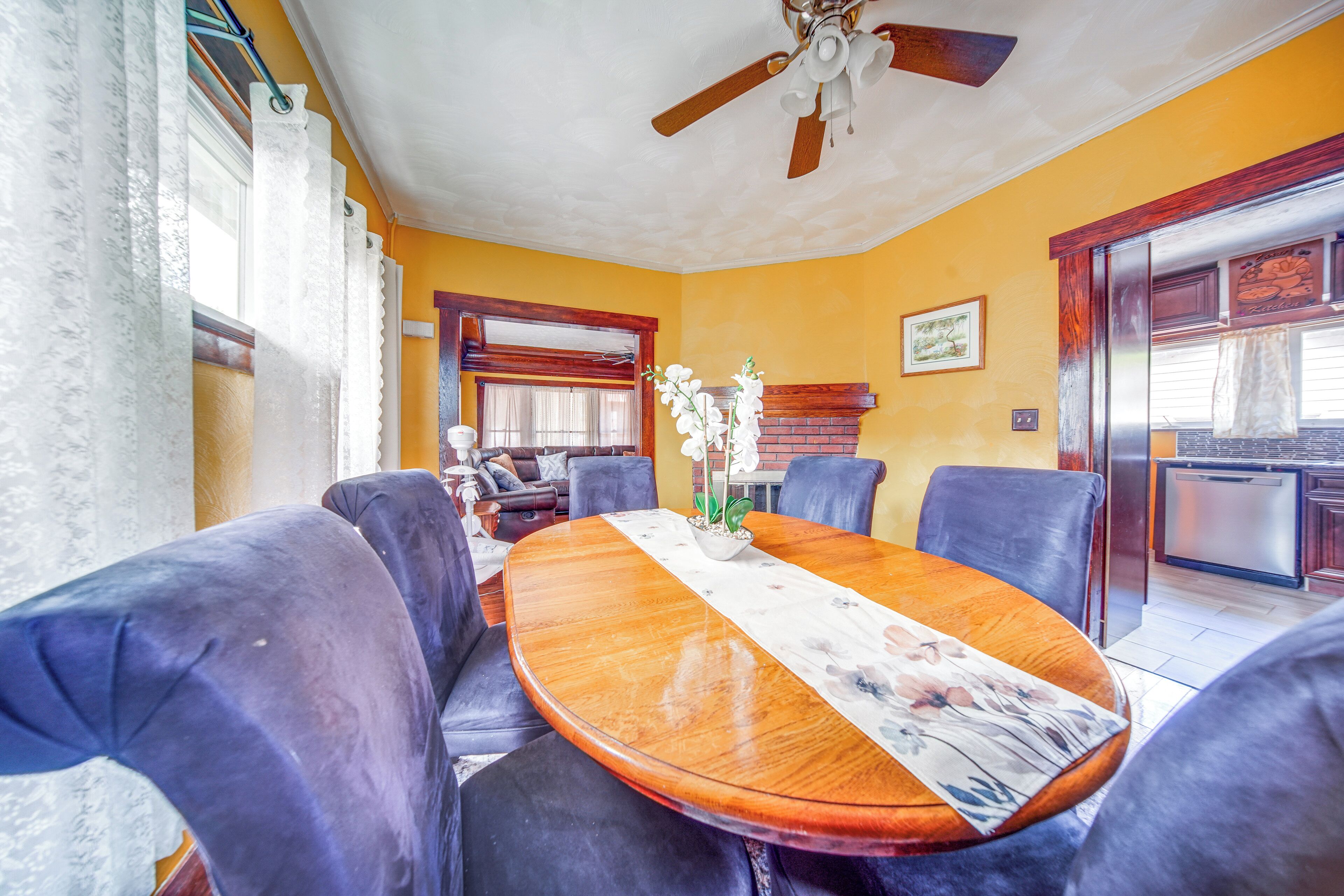 Un comedor con una mesa de madera, sillas tapizadas en azul, un ventilador de techo y una chimenea de ladrillo.