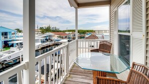 A covered outdoor area with a glass table and wicker chairs, overlooking a marina with boats. - Canal-front Key Largo Retreat w/ Community Beach! (Key Largo)