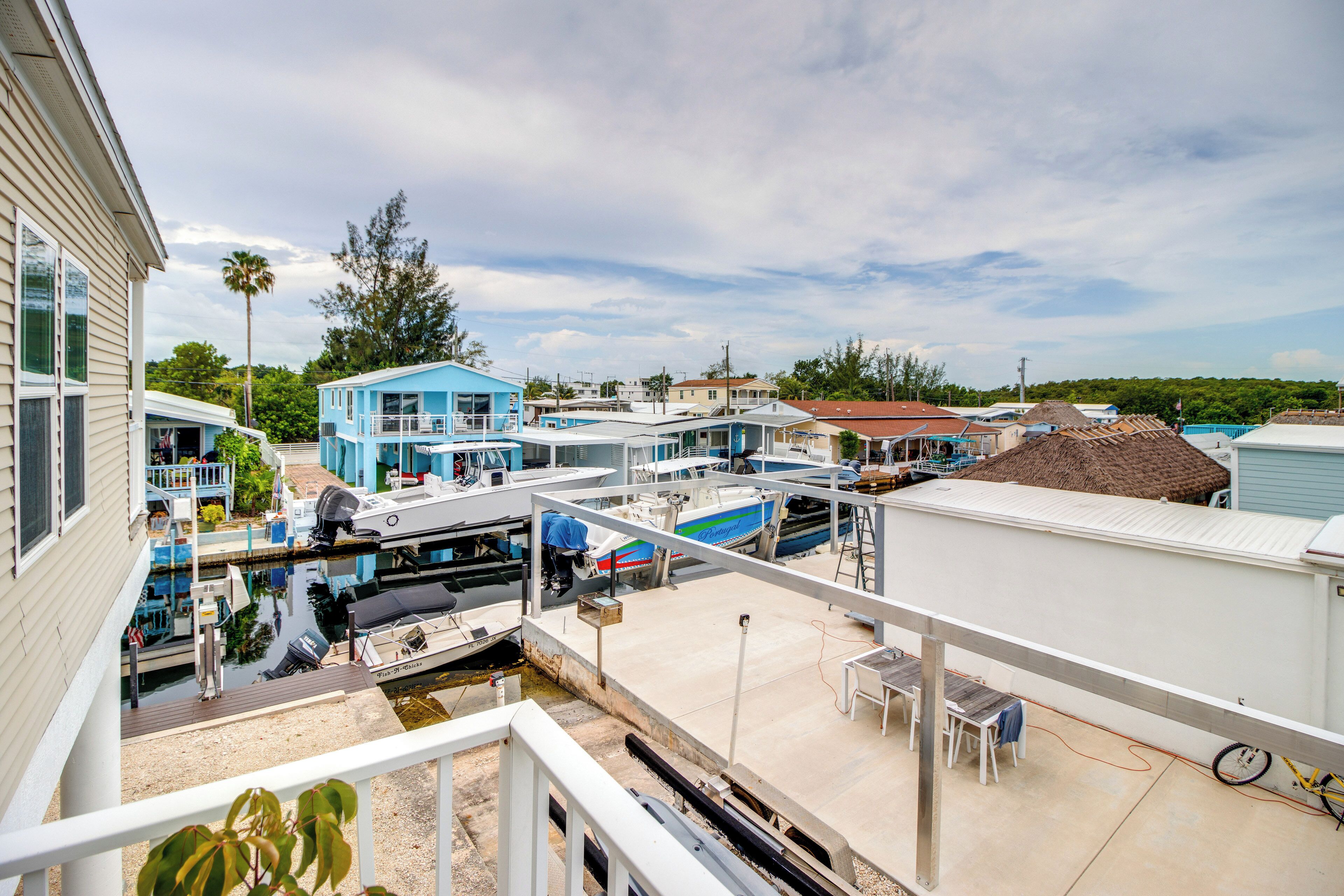Uma marina com barcos atracados, uma pequena área de cais com uma mesa e cadeiras, e um edifício com fachada azul.