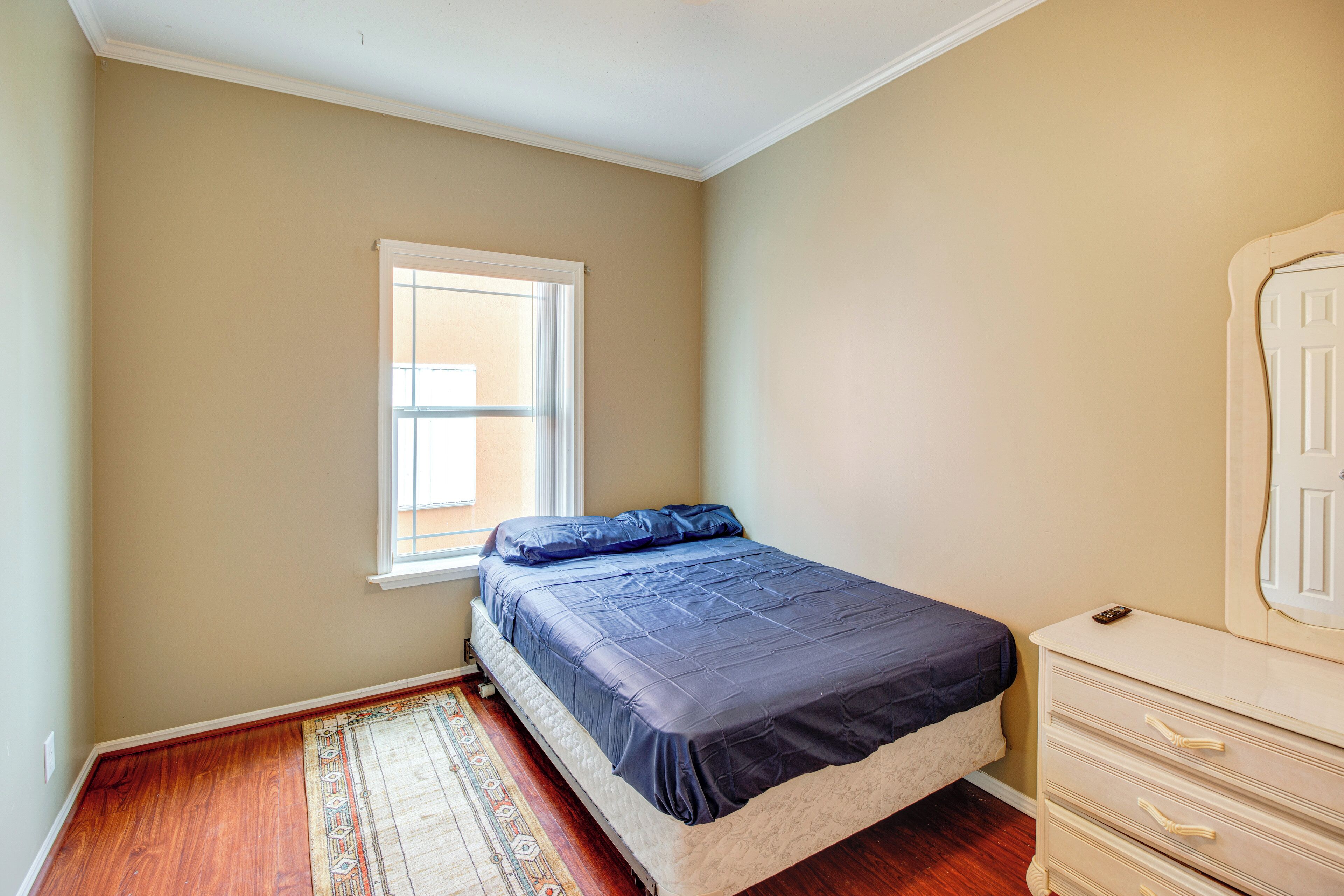 Quarto com cama, cômoda, janela e tapete estampado.