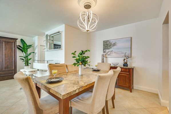 A dining area with a marble table, beige chairs, a potted plant, and a chandelier. - Hollywood Condo w/ Beach Access - Walk to Shore! (Hollywood)