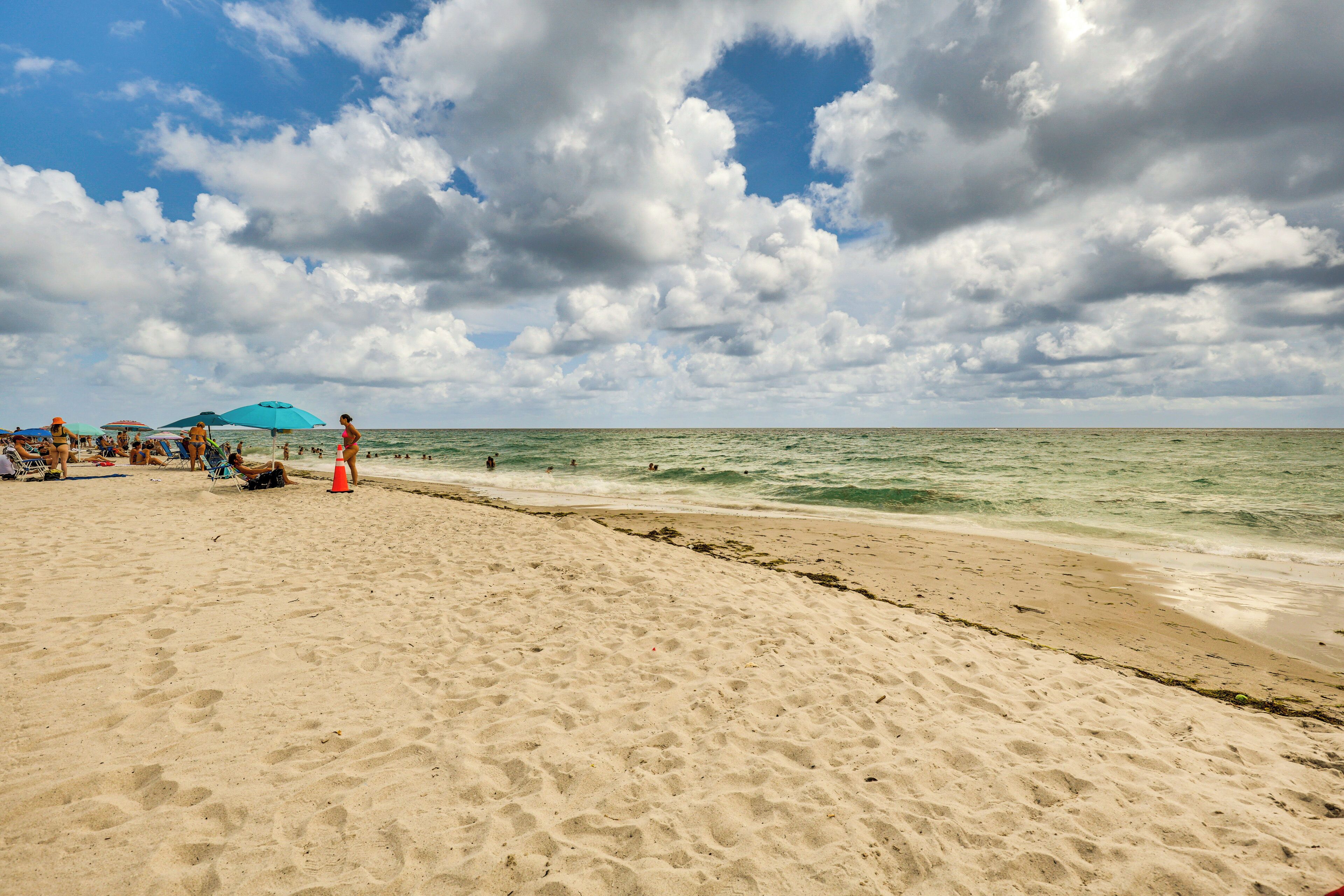 A sandy beach with umbrellas and people.