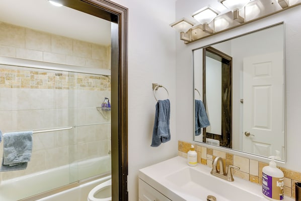 A modern bathroom with a glass shower enclosure, a white sink with a mirror above it, and a towel rack with a blue towel.