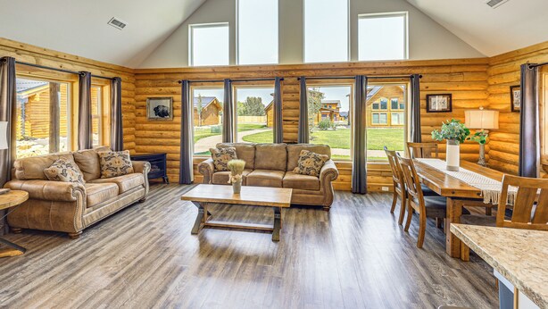 A log cabin interior with a wooden floor, a sofa, a coffee table, and a dining table with chairs.