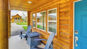 A log cabin with a blue door, two Adirondack chairs, and a table outside.