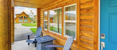 Une cabane en rondins avec une porte bleue, deux fauteuils Adirondack et une table à l’extérieur.