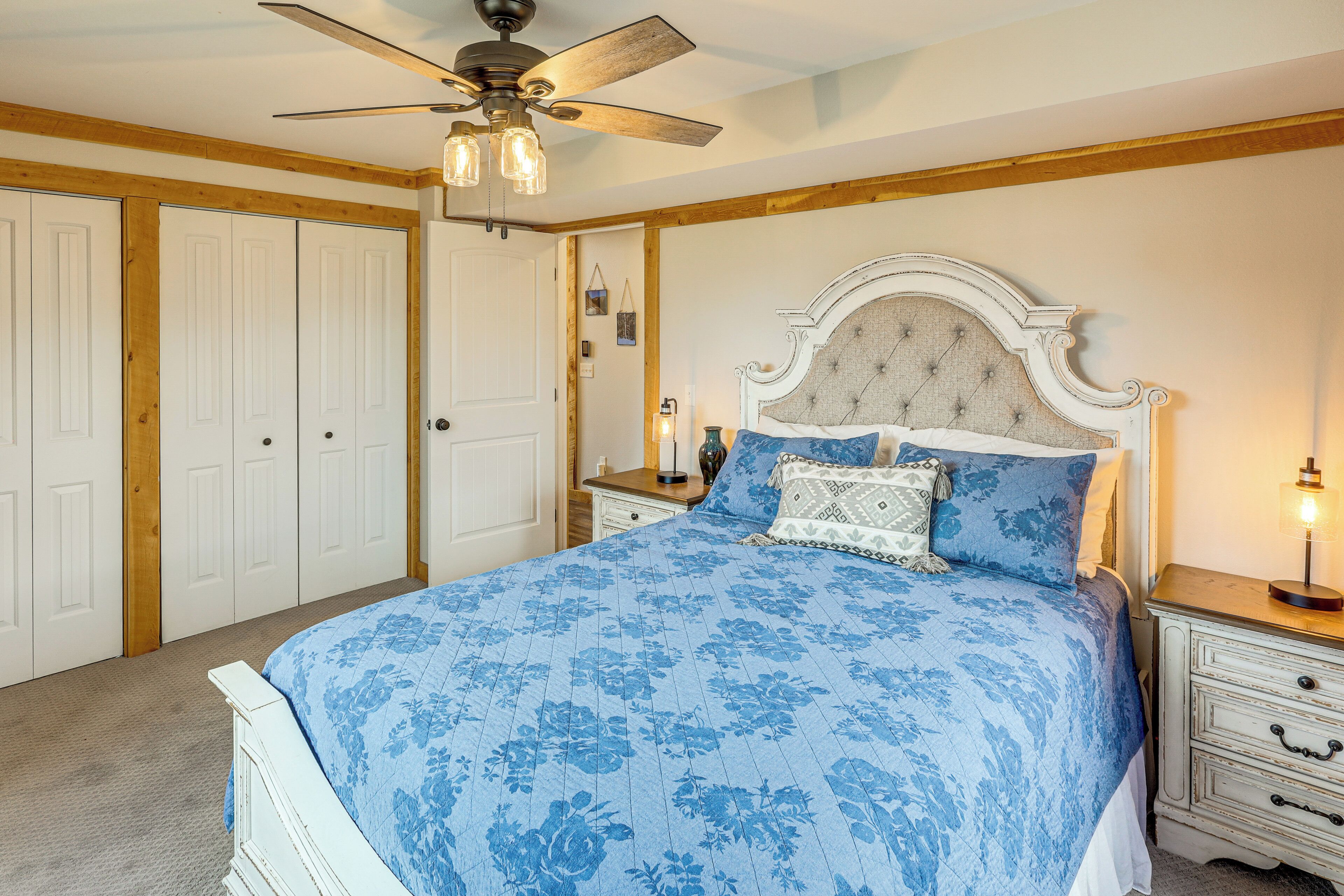 A bedroom with a large bed, a ceiling fan, wooden paneling, and a nightstand with a lamp.