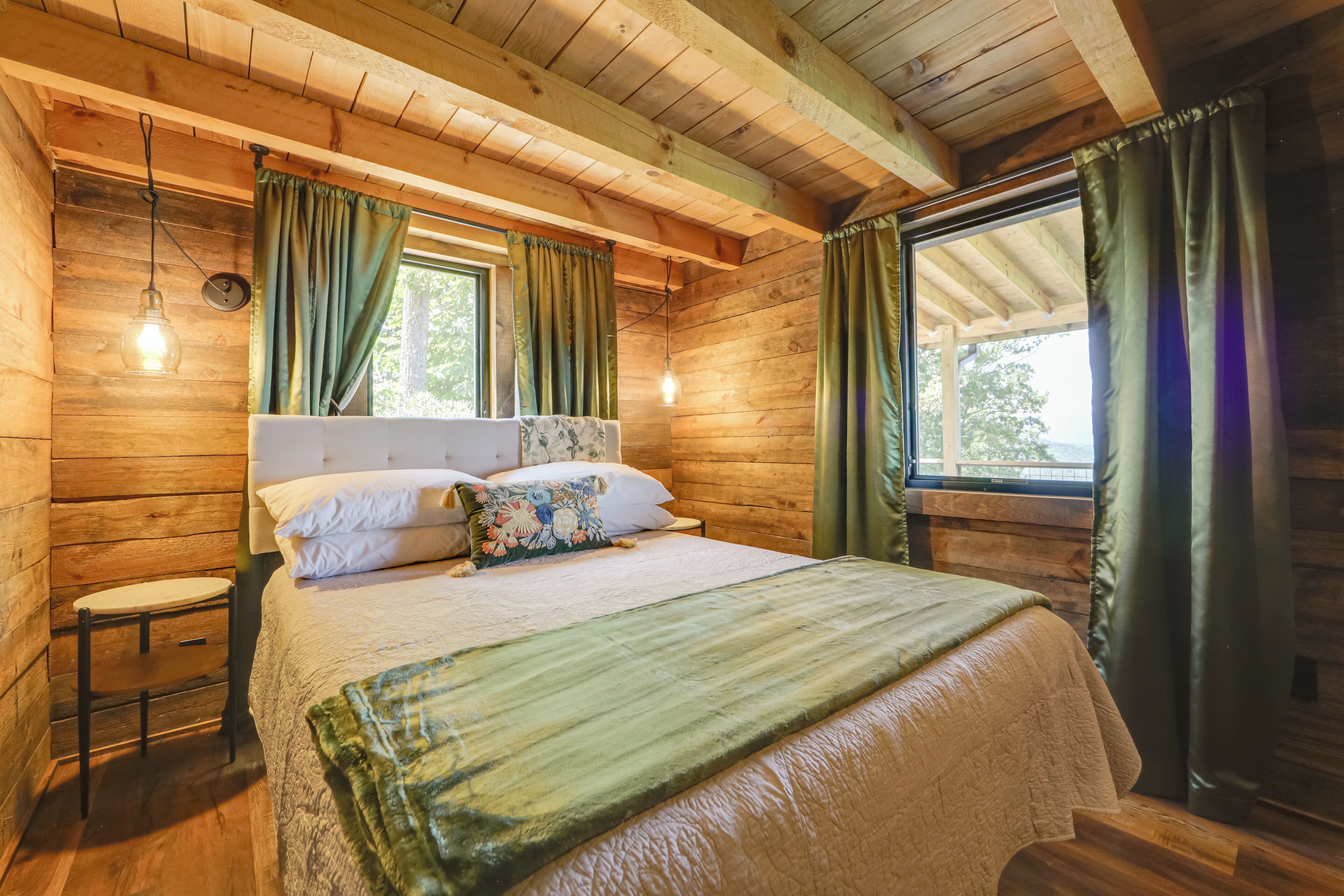 A wooden cabin bedroom with a bed, a nightstand, and a window with curtains.