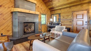 Un intérieur de chalet chaleureux avec une cheminée, des murs en bois, un canapé et un coin repas.