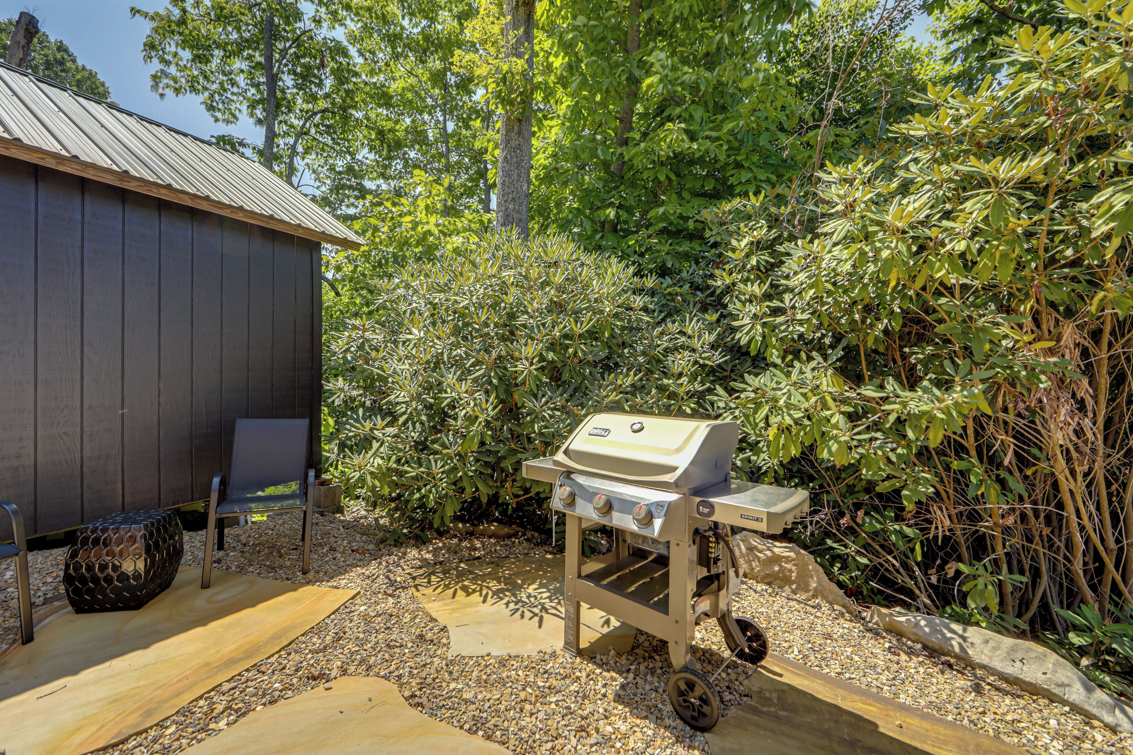 A barbecue grill in a garden area with a wooden bench and a shed in the background.