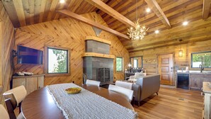 L’intérieur d’un chalet en bois comprend un coin repas, un canapé, une cheminée et une cuisine.