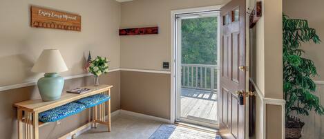 A hallway with a wooden bench, a lamp, a welcome sign, and a door leading to a balcony.