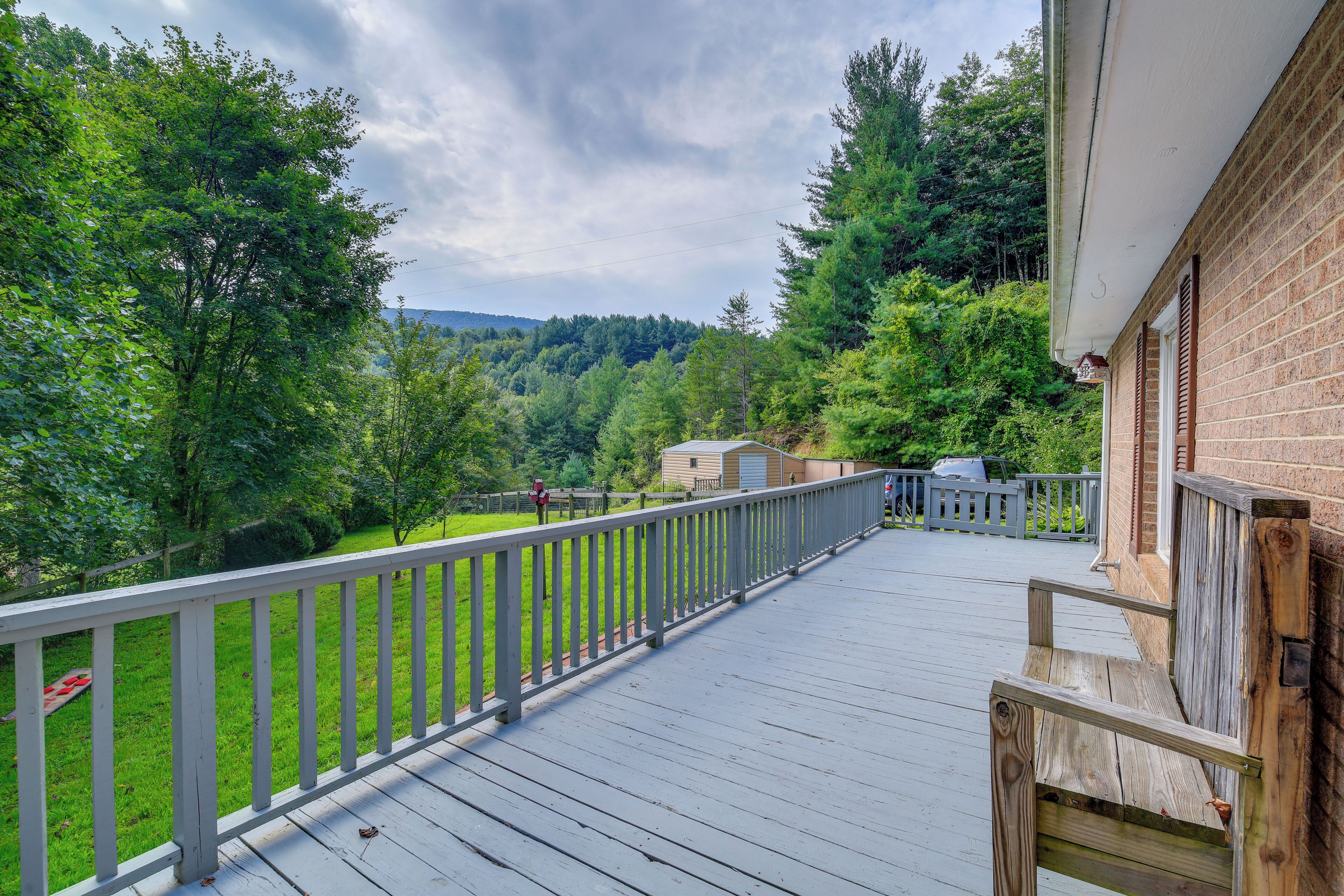 A wooden deck with a railing overlooking a green landscape and a building with a brick exterior.