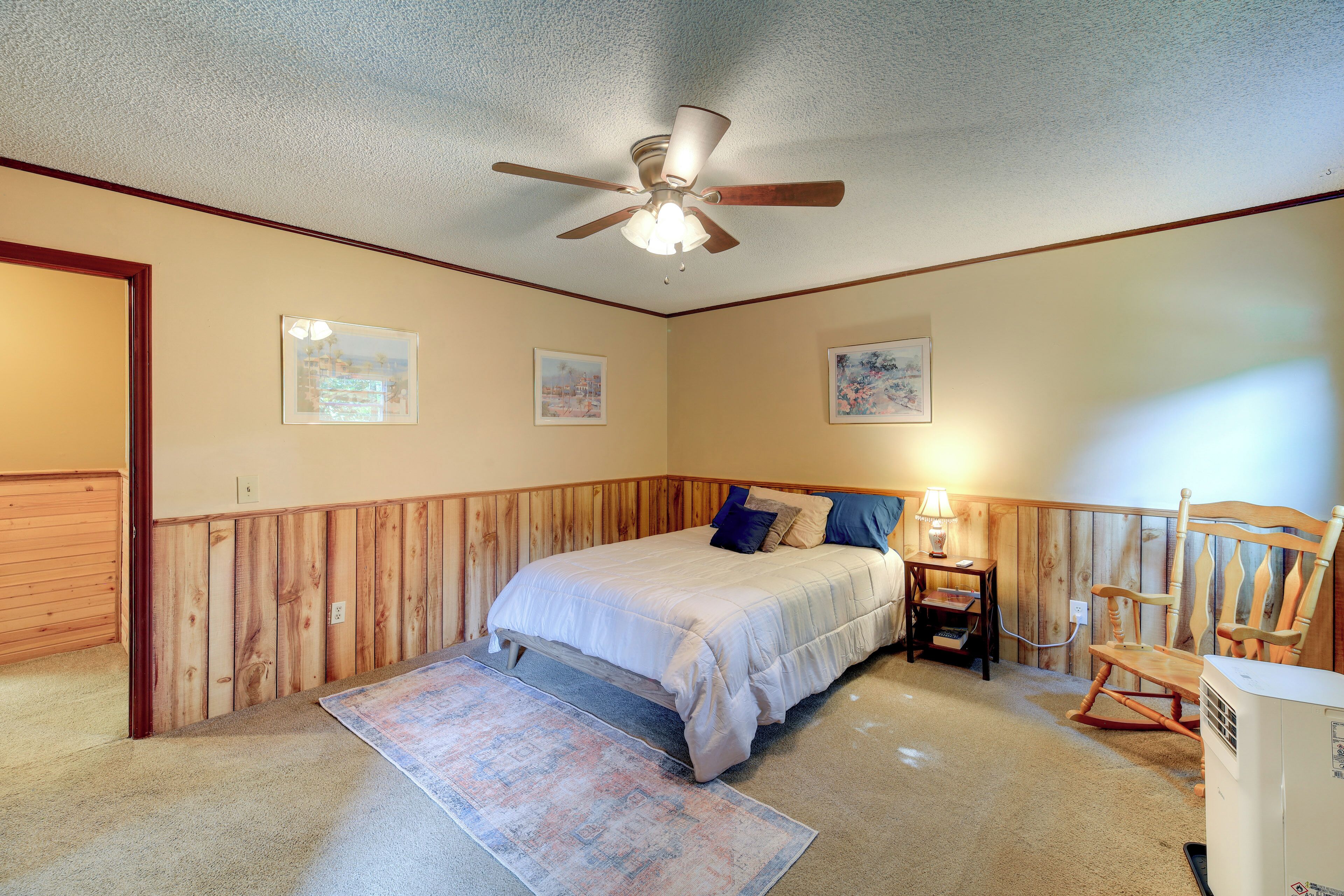 A bedroom with a bed, a ceiling fan, a rocking chair, and a heater.