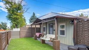 A covered patio area with a swing seat, a table with a pink tablecloth, and a brick wall. - Aurora Abode: 7 Mi to Dtwn Denver! (Aurora)