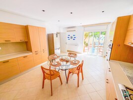 Una cocina moderna con armarios de madera, una mesa de comedor de cristal con cuatro sillas y vistas al patio exterior.