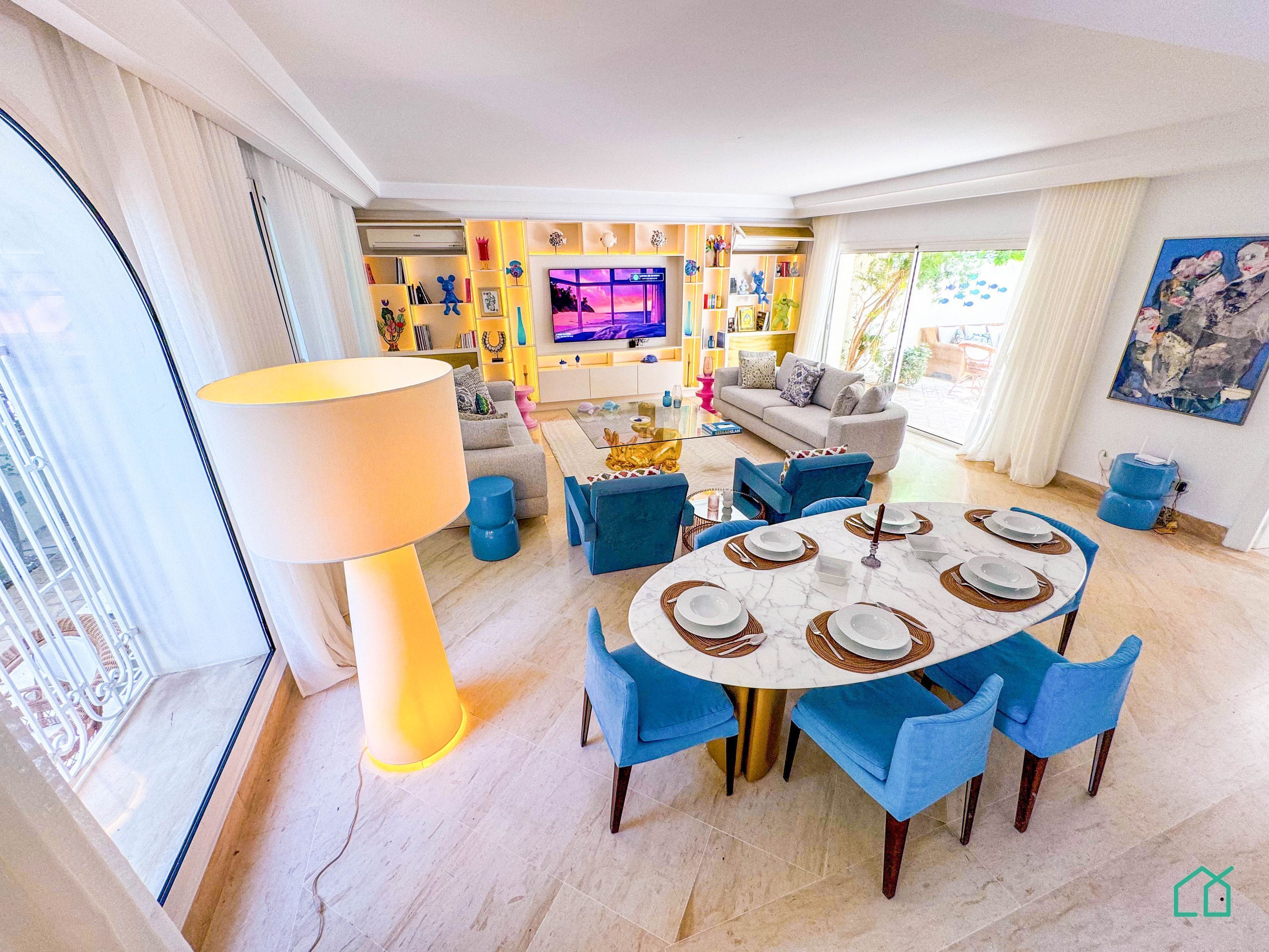 A modern living room with a dining area, a large TV, and a bookshelf.