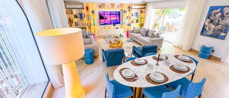 A modern living room with a dining area, a large TV, and a bookshelf.