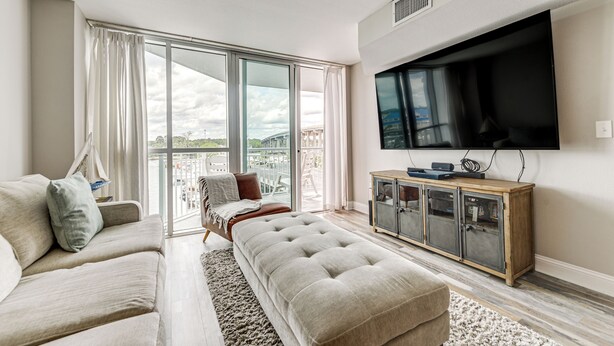 A modern living room with a large window, a sofa, a coffee table, and a flat-screen TV mounted on the wall.