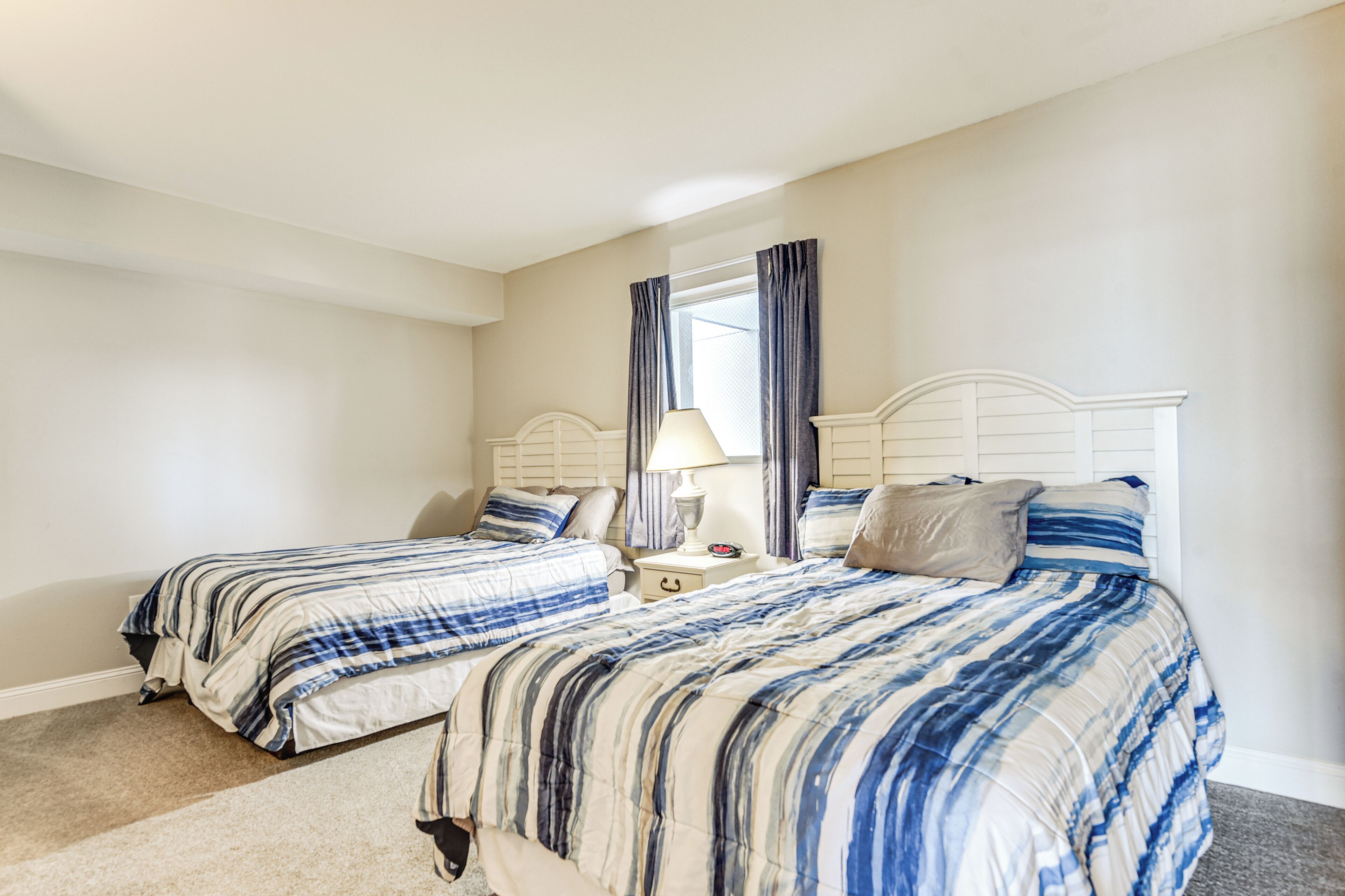 A bedroom with two beds, a nightstand, a lamp, and a window with curtains.