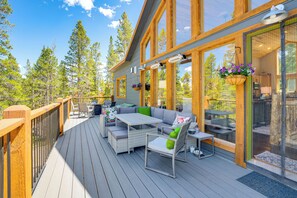Eine Holzterrasse mit Gartenmöbeln, großen Fenstern und hängenden Blumenkörben.