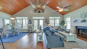 A spacious living room with a high ceiling, wooden beams, a fireplace, and a dining area with a blue rug. - Riverfront Aurora Home w/ Deck & Private Pier! (Aurora)