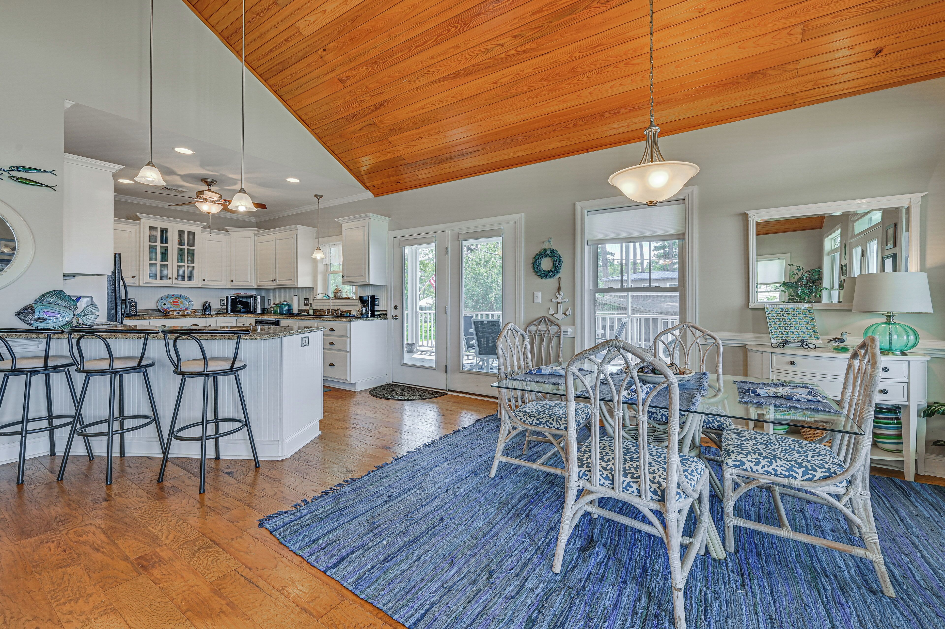 A spacious kitchen with white cabinets, a wooden ceiling, and a dining area with wicker chairs and a glass table.