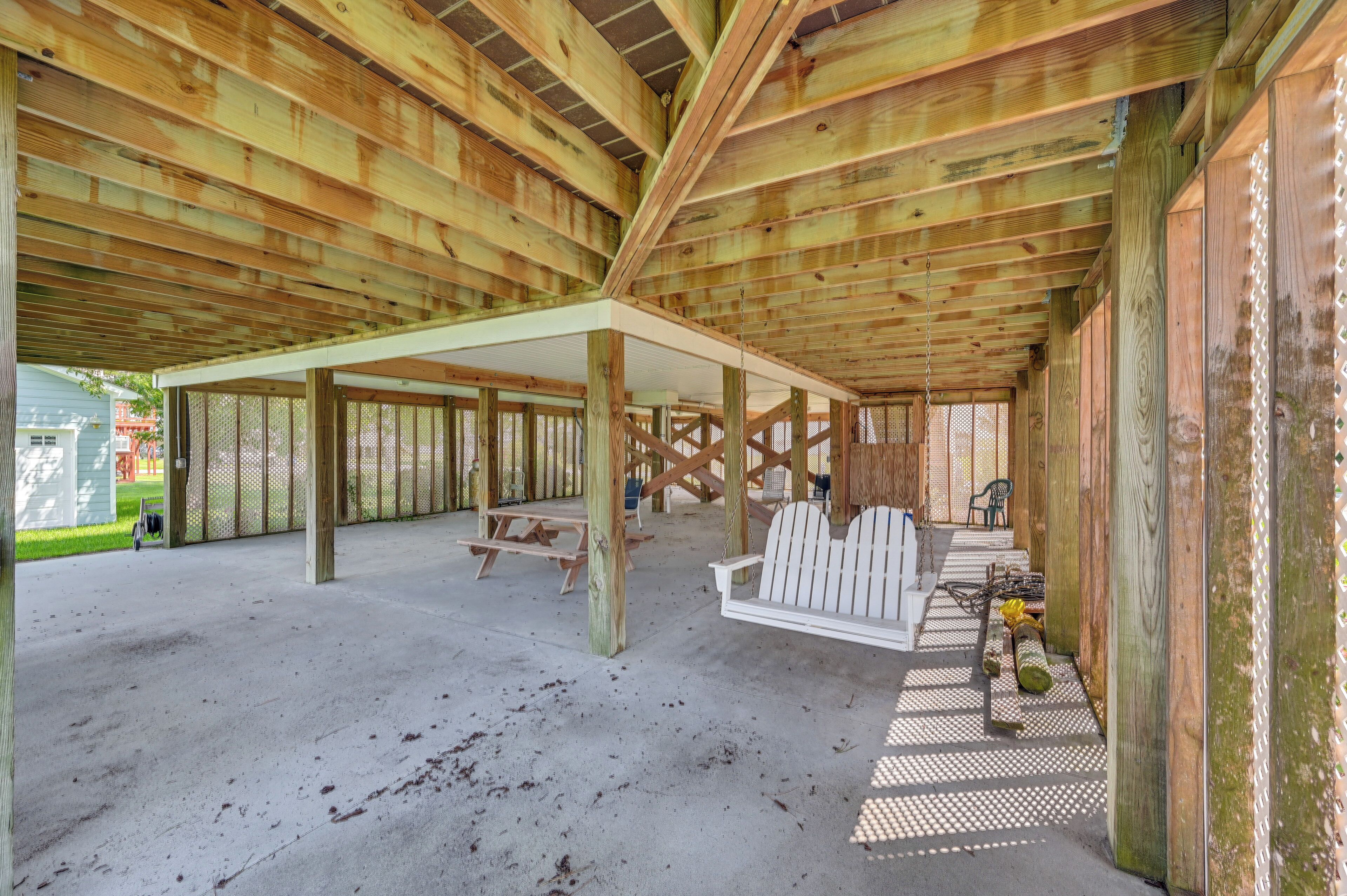 A covered outdoor area with wooden beams, a picnic table, and Adirondack chairs.