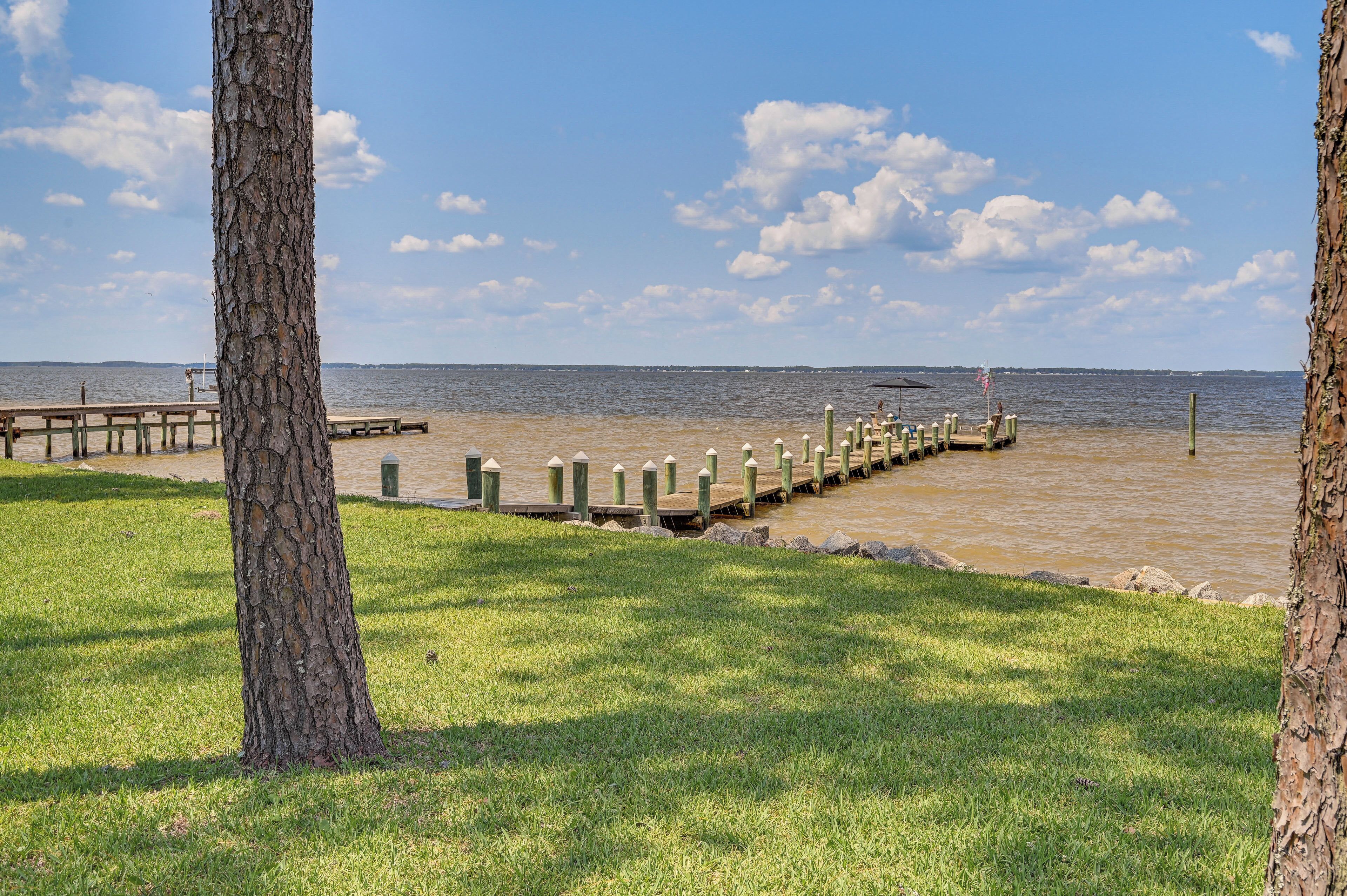 A lakeside park with a wooden dock extending into the water, surrounded by grassy areas and trees.