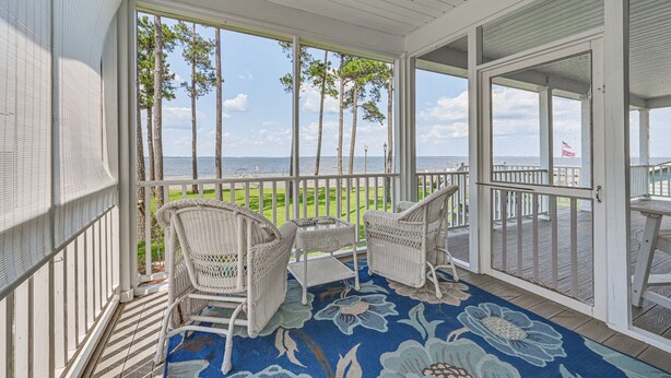 A covered porch with wicker chairs and a table, overlooking a grassy area and the sea. - Riverfront Aurora Home w/ Deck & Private Pier! (Aurora)