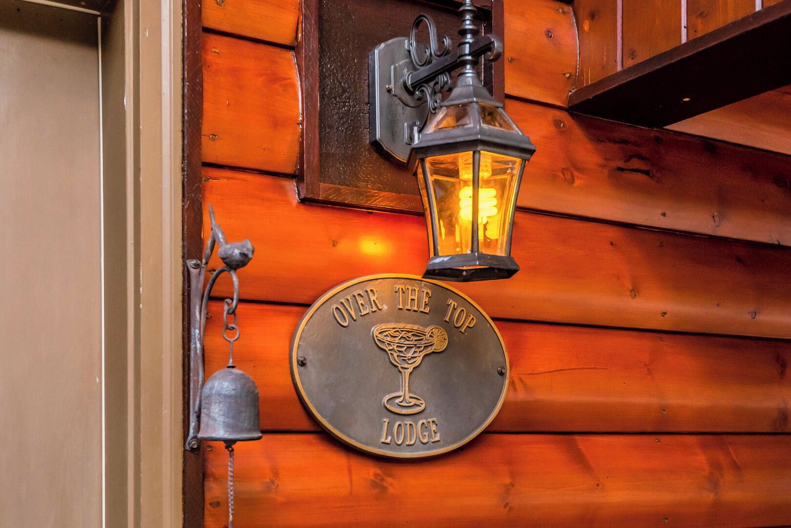 En dörr av trä med en skylt som lyder ”OVER THE TOP LODGE” och en tänd lykta ovanför.