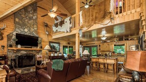 A spacious lodge with a stone fireplace, leather seating, a kitchen area, and a dining space. - Appalachian Mtn Cabin Near New River State Park! (Piney Creek)
