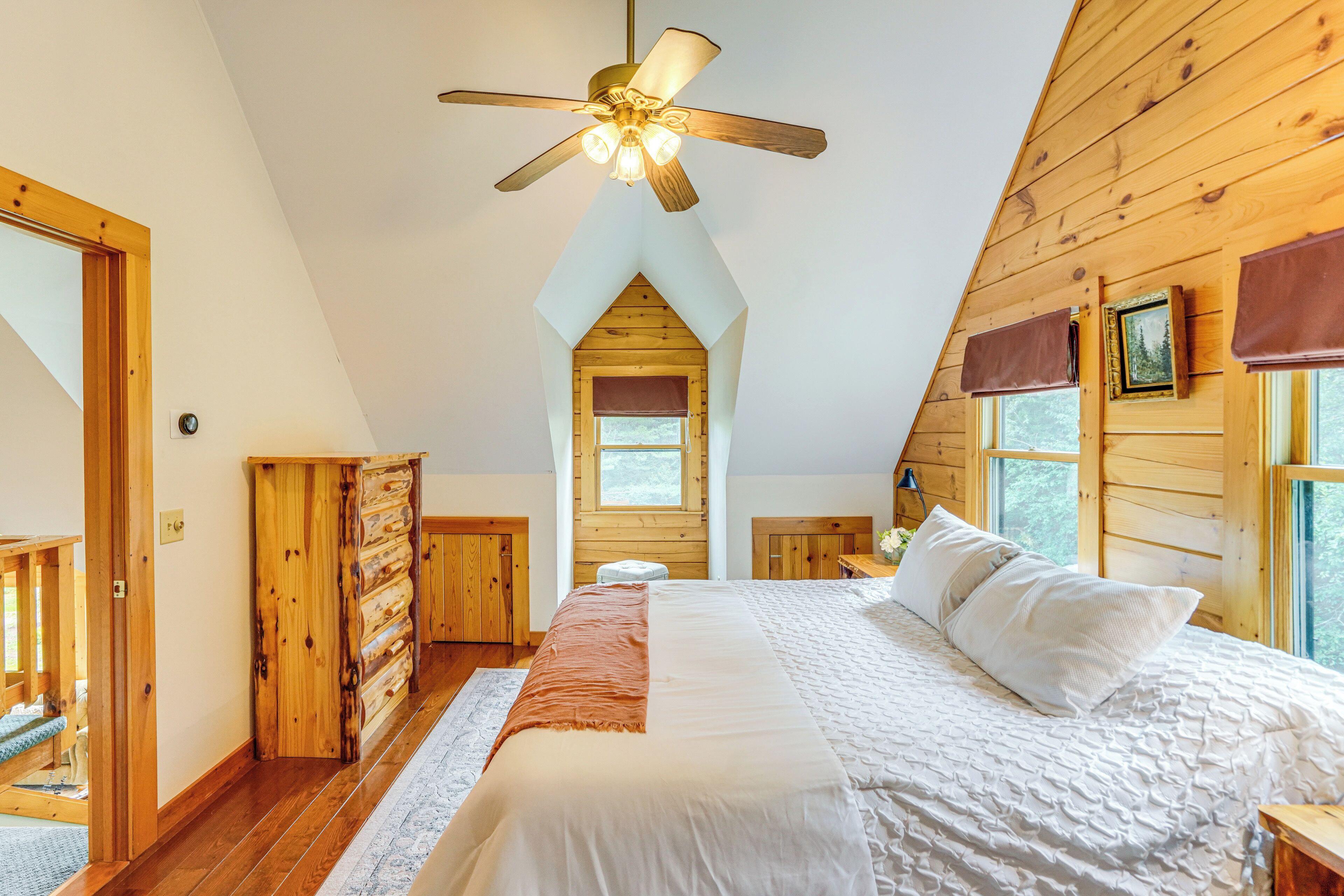 Un dormitorio con una cama grande, paredes de madera, un ventilador de techo y una ventana.
