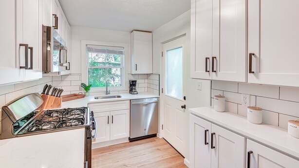 A modern kitchen with white cabinets, a stainless steel stove, and a dishwasher.