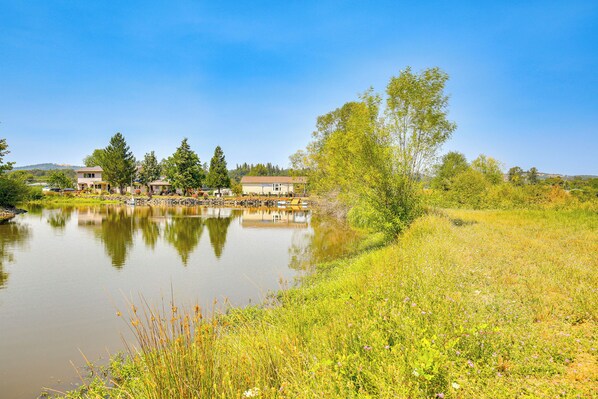 A lakeside view with buildings, trees, and a grassy area. - Southern Oregon Cabin: Fire Pit & Private Pond! (Oakland)