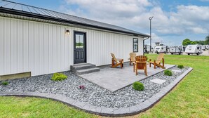 A white building with a black door, a small porch with wooden chairs and a table, and a gravel pathway leading to the door. - Charming Middlebury Retreat w/ Patio & Fire Pit (Middlebury)