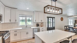 A modern kitchen with white cabinetry, a central island, and a dining area with a table and chairs. - Charming Middlebury Retreat w/ Patio & Fire Pit (Middlebury)