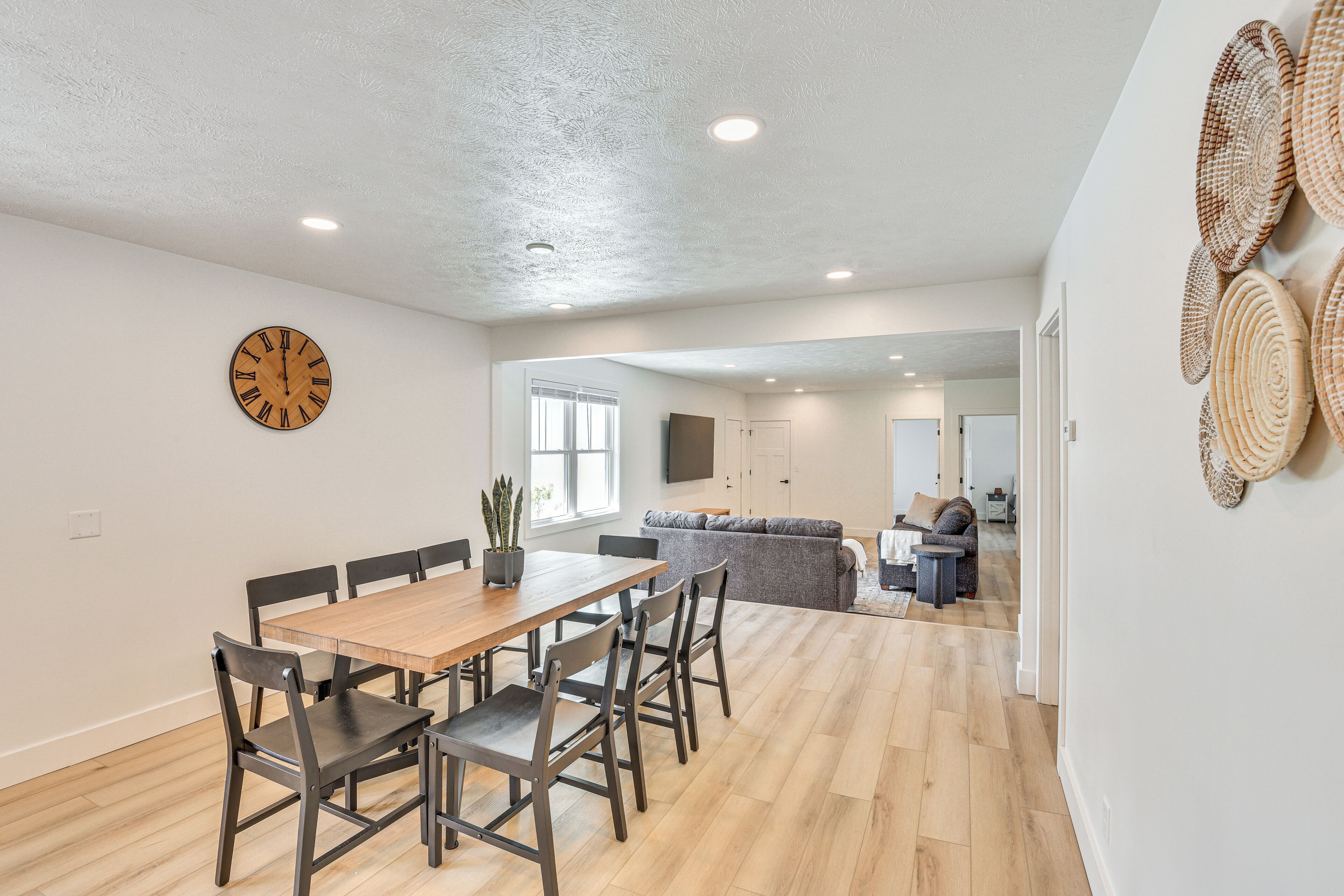 Un comedor espacioso con una mesa y sillas de madera, un reloj de pared y una cocina al fondo.