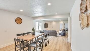 Un comedor espacioso con una mesa y sillas de madera, un reloj de pared y una cocina al fondo.