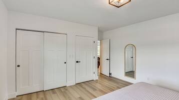 A bedroom with a large bed, two white doors, a mirror, and a wooden floor.