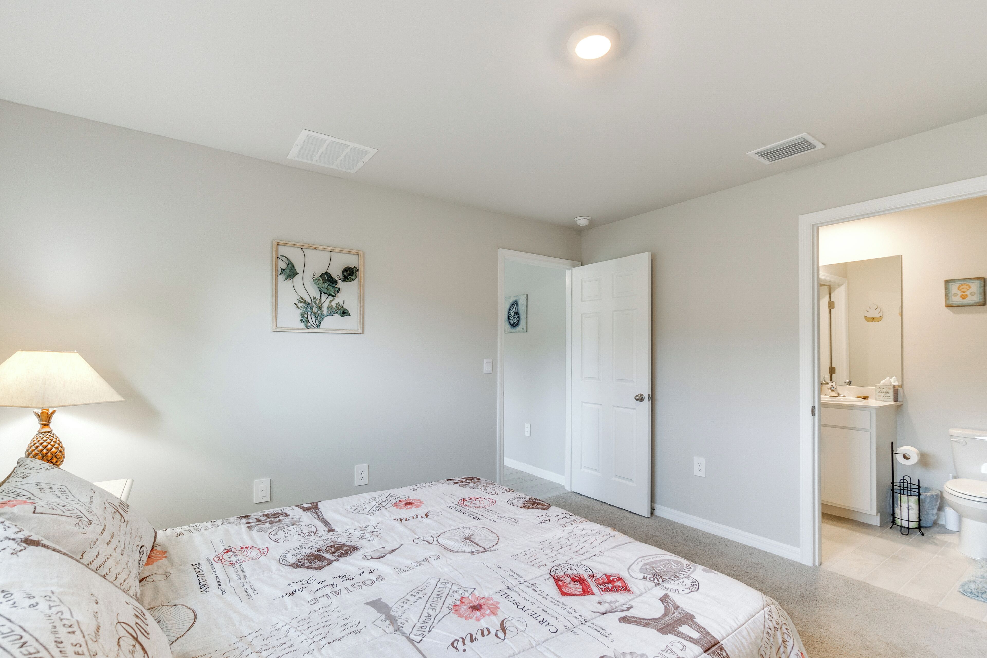 A bedroom with a bed, a nightstand, a lamp, a door, and a bathroom visible through an open door.