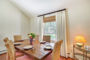 A dining room with a wooden table set for four, wicker chairs, a vase with flowers, and a lamp on a side table. - 2 Mi to Aiken Horse Park: South Carolina Apt (Aiken)