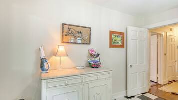 A hallway with a white door, a checkered floor, a white cabinet with drawers, a lamp, and two framed pictures on the wall.