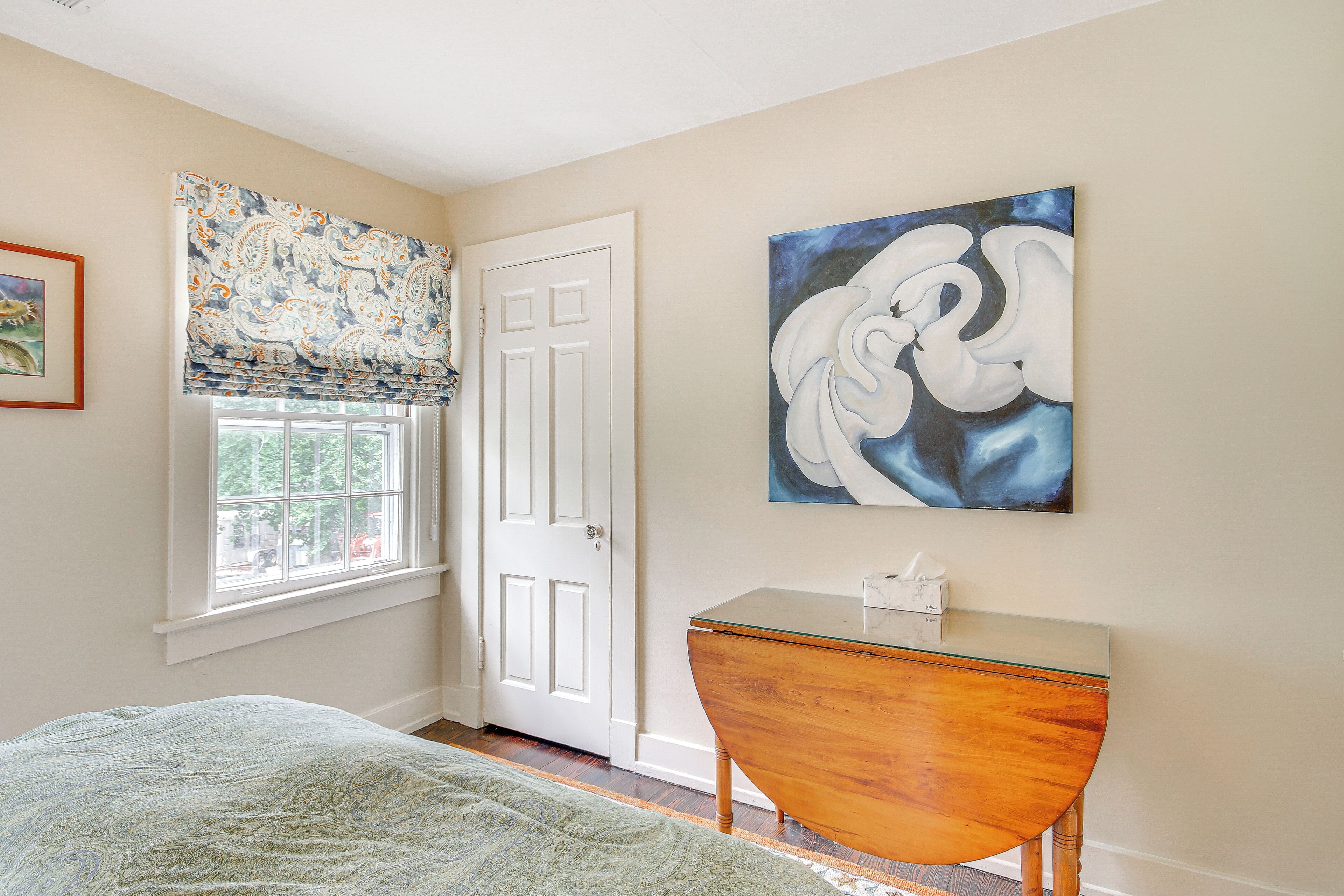 Un dormitorio con cama, ventana con vistas, una puerta y un cuadro en la pared.