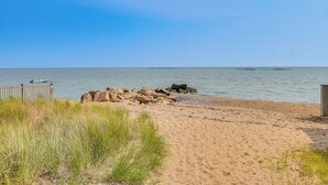 A sandy beach with a wooden fence and rocks, leading to a calm sea. - Walk to Beaches: Sunny East Haven Home w/ Grill (East Haven)