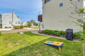A residential lawn with a lawnmower, a barbecue grill, and a wooden board game. - Walk to Beaches: Sunny East Haven Home w/ Yard (East Haven)