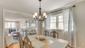A dining area with a wooden table, chairs, and a chandelier. There is a sofa and a coffee table in the background. - Walk to Beaches: Sunny East Haven Home w/ Grill (East Haven)